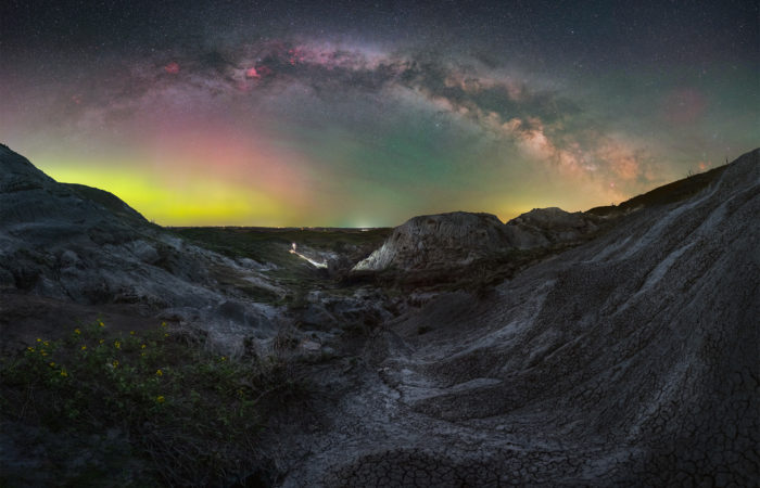 The milky way arch over badlands in saskatchewan with a portrait of a night photographer